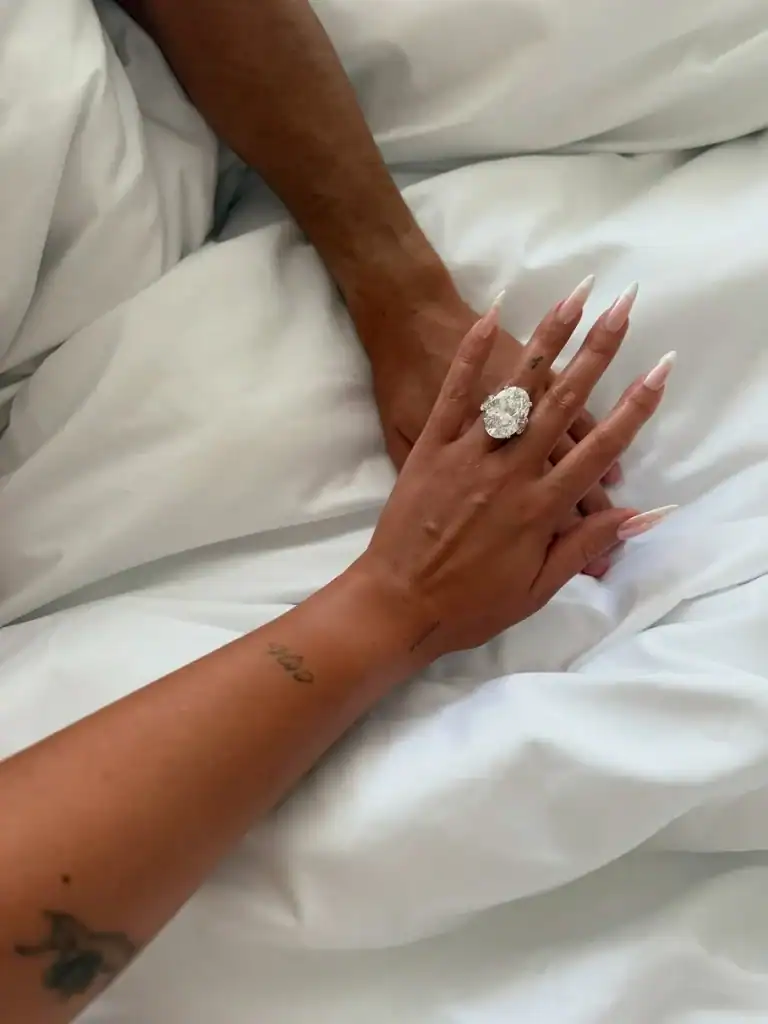 الأبصار تلتقي بأيدٍ مرتدية خواتم ماسية على سرير أبيض أنيق.